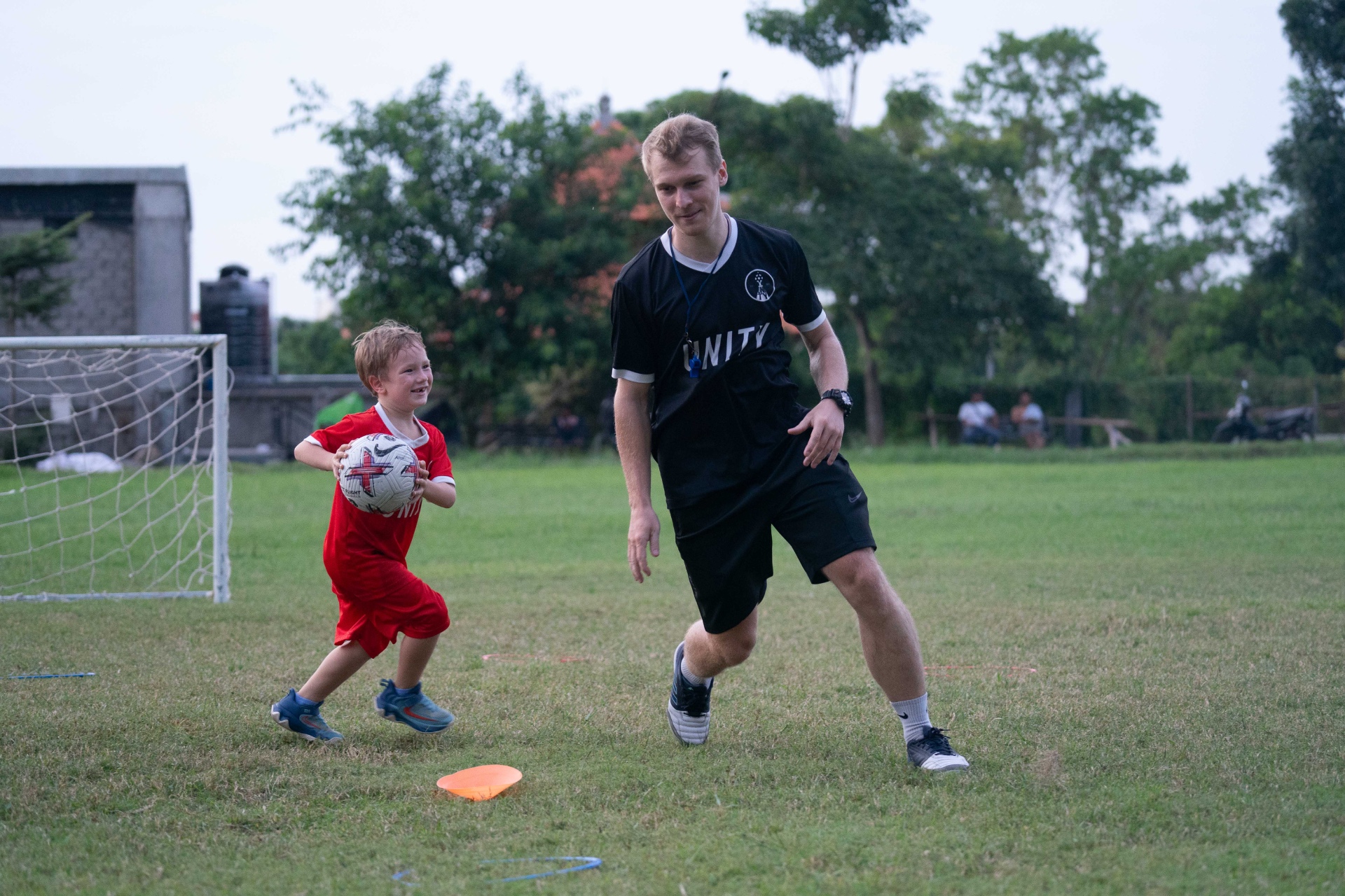 Child in a red UNITY kit playing football with his coach