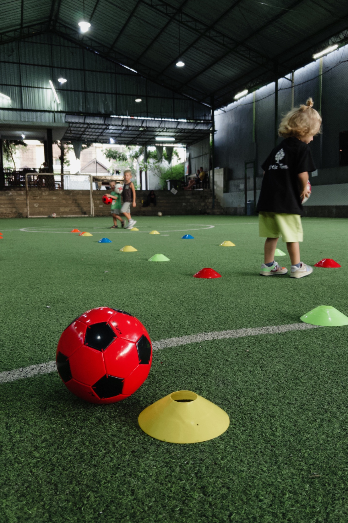 Young children practising with balls and cones on an indoor pitch